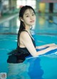 A woman in a black bathing suit sitting on a surfboard in a pool.