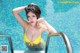 A woman in a yellow bikini posing by a swimming pool.